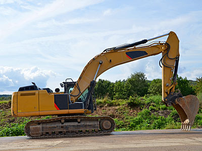Ein Bagger steht auf einer Baustelle, umgeben von Grün.