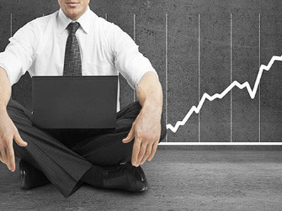 Ein Mann in einem Anzug sitzt mit einem Laptop und einem Diagramm mit steigenden Linien im Hintergrund.